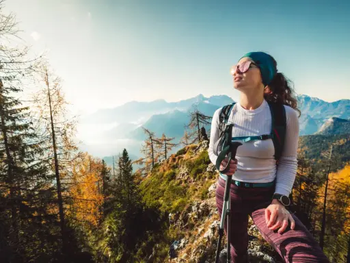 Kobieta w sportowym outfit w górach, z kijkami trekkingowymi, podziwia jesienny krajobraz.