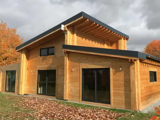 Une belle maison en bois, prête à accueillir ses habitants. L'automne arrive, les feuilles tombent autour de cette construction chaleureuse.