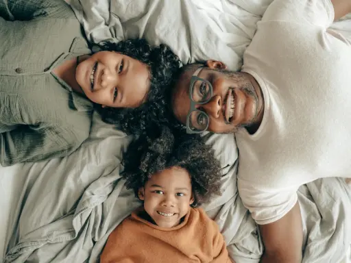 Un padre e i suoi due figli sorridono sdraiati sul letto, creando delle foto di famiglia originali e piene d'amore.