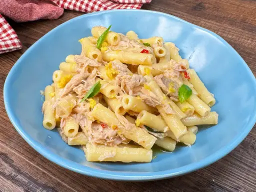 Piatto di pasta tonno e limone, condita con tonno sfilacciato, scorza di limone e basilico fresco, servita in un piatto blu.