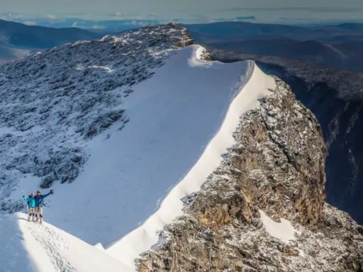 Två personer firar på toppen efter att ha lyckats bestiga Kebnekaise. Snö och sten dominerar landskapet.
