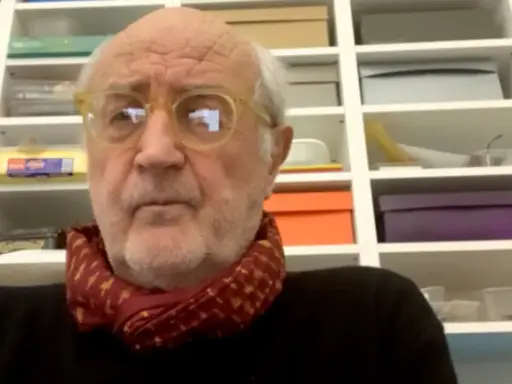 Ritratto di Francesco Pecoraro con occhiali gialli e sciarpa rossa, davanti a una libreria piena di scatole.