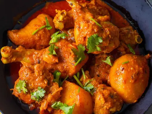 Un plat appétissant de poulet au curry, avec des morceaux de poulet tendres et des pommes de terre dans une sauce épicée, garni de coriandre fraîche.