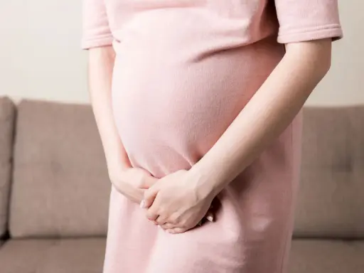 Kobieta w ciąży w różowej sukience trzyma ręce na brzuchu, doświadczając dyskomfortu związanego z nietrzymaniem moczu w ciąży.