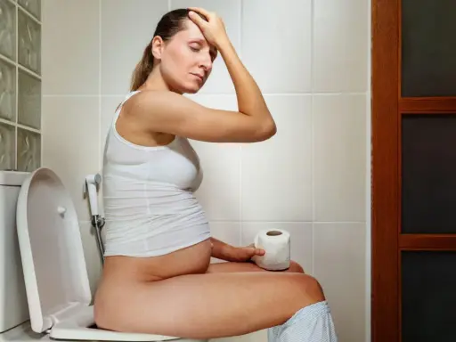 Donna incinta sul water, con la mano sulla fronte, preoccupata per la cacca in gravidanza.
