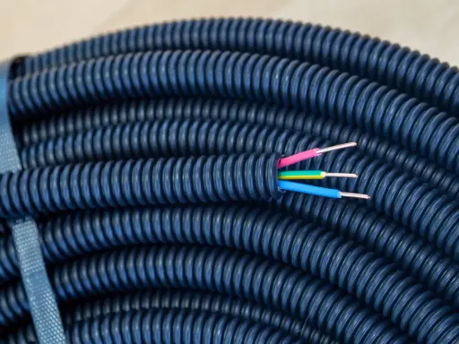 Gaine électrique bleue enroulée, prête pour une installation dans le jardin. Trois fils colorés (rose, jaune, bleu) émergent de son extrémité, suggérant la profondeur de son utilité.
