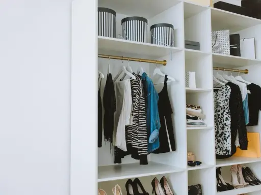 Un armario organizado con ropa colgada y doblada, cajas a rayas y bolsas de compras. Una guía visual de como organizar un armario de forma elegante.