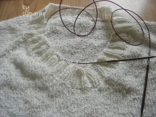 Biały sweter w trakcie dziergania, widoczny fragment kołnierza i druty. Jak zrobić kołnierz do swetra na drutach?