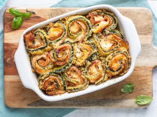 Involtini di zucchine al forno, ripieni di prosciutto e formaggio, dorati e croccanti, guarniti con basilico fresco.
