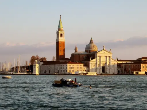Le campanile et l'église de San Giorgio Maggiore à Venise se reflètent sur l'eau. Un bateau transporte des passagers.