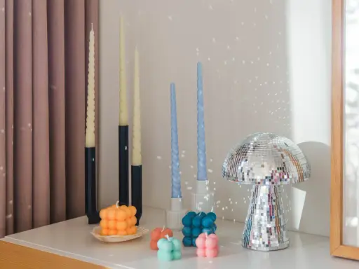 En samling av DIY ljus i olika former och färger, inklusive bubbel- och vridna ljus, samt en glittrig svampformad dekoration.