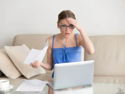 Zmartwiona kobieta z okularami sprawdza dokumenty na laptopie, martwiąc się o przedawnienie długu za czynsz mieszkaniowy.