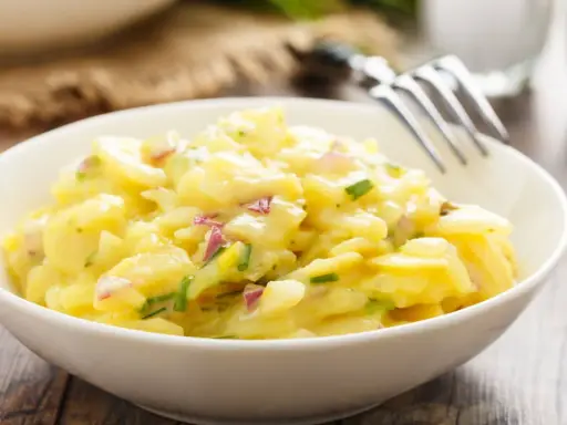 Schüssel mit cremigem Kartoffelsalat, garniert mit roten Zwiebeln und Schnittlauch. Ein köstliches Rezept für Kartoffelsalat!