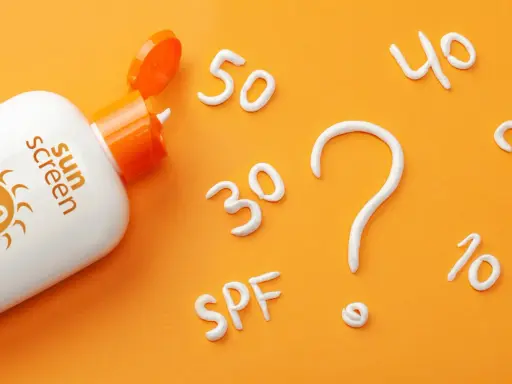 Flacon de crème solaire SPF 50 ouvert, avec des chiffres (30, 40, 20, 10) et un point d'interrogation formés en crème. Quel indice choisir ?
