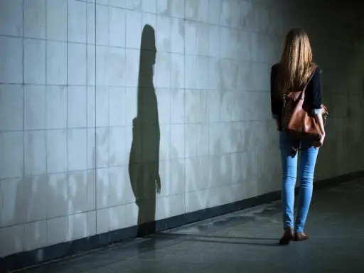 Dziewczyna z plecakiem idzie przez tunel, jej cień na ścianie symbolizuje dyfuzję odpowiedzialności.
