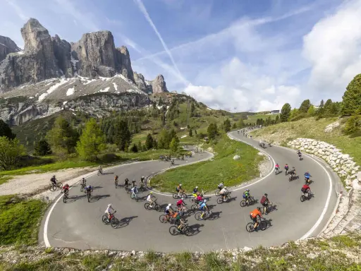 Ciclisti affrontano tornanti in una spettacolare salita alpe d'Huez, con maestose montagne sullo sfondo.