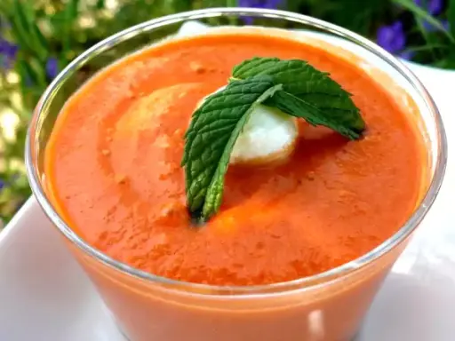 Un verre de gaspacho tomate, garni d'une feuille de menthe et d'une boule de mozzarella. Parfait pour se rafraîchir.