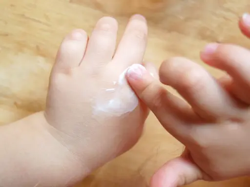 Mani di bambino applicano crema, un gesto che aiuta a contrastare la pelle atopica, alleviando secchezza e prurito.