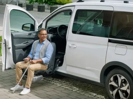 Hombre sonriente sentado en un asiento elevador de coche, listo para salir. Un ejemplo de soluciones de movilidad accesibles.