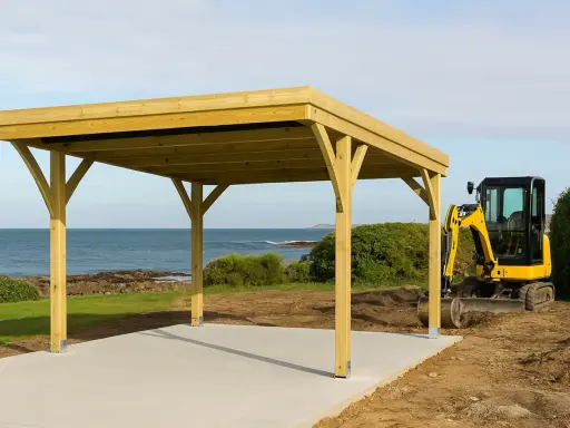 Un carport en bois est en cours de construction près de la mer. Une mini-pelle jaune est garée à côté, prête pour la suite des travaux. Une déclaration de carport est nécessaire pour ce projet.