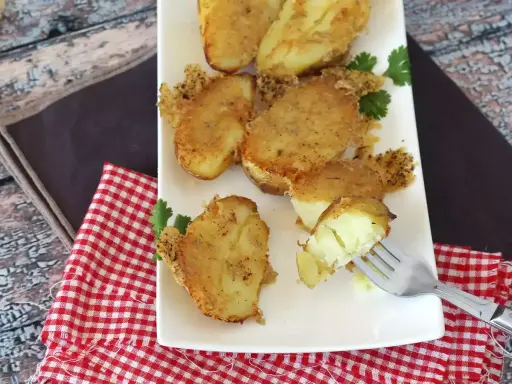 Krispiga, gyllene bitar av confiterad potatis, perfekt tillagade och serverade på en vit tallrik med en gaffel som visar den mjuka insidan.