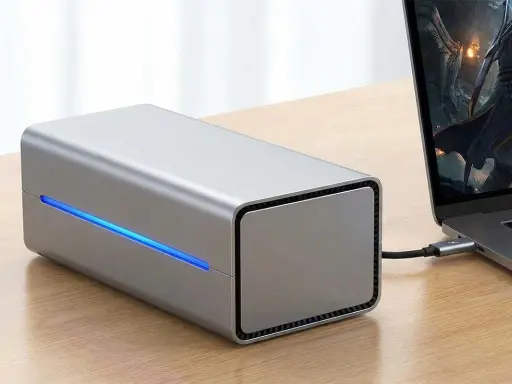Srebrna obudowa egpu do laptopa z niebieskim podświetleniem, podłączona do laptopa z grą na ekranie.