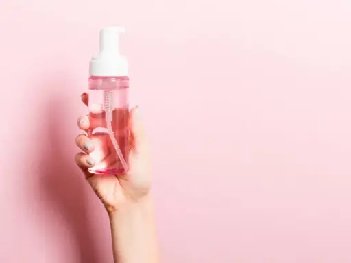 Mano sostiene botella de agua micelar con dispensador. ¡Perfecto para cuando el agua micelar se enjuaga!