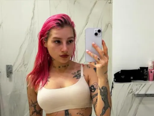 Młoda Leosia z kolorowymi włosami i licznymi tatuażami na ciele robi sobie selfie w łazience.