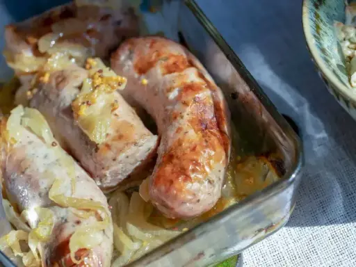 Aromatyczna, pieczona biała kiełbasa z cebulką i musztardą w szklanym naczyniu.