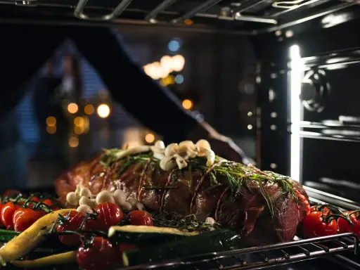 Ein Braten mit Kräutern, Knoblauch, Tomaten und Zucchini wird in den Ofen geschoben. So wird ein Dialoggarer zum Leben erweckt.