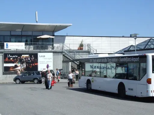 Autobus wahadłowy na lotnisko Oslo Torp. Ludzie z bagażami wychodzą z terminala.