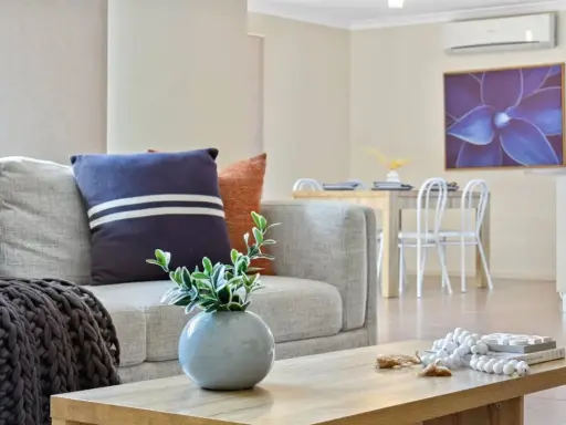 Soggiorno moderno con divano grigio, cuscini decorativi e un condizionatore per rendere smart l'ambiente. Tavolo da pranzo e quadro floreale sullo sfondo.
