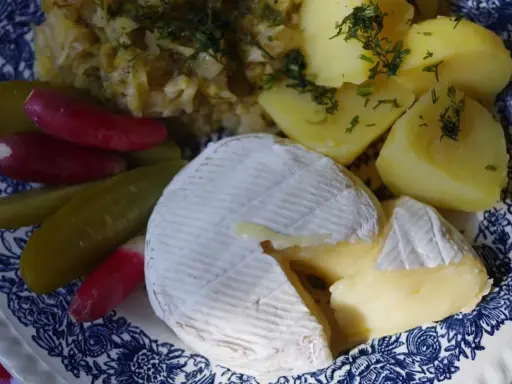 Częściowo roztopiony camembert z ziemniakami, ogórkami kiszonymi i rzodkiewką na talerzu.