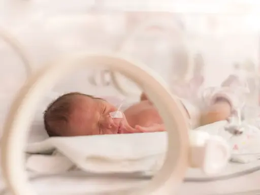 Maleńki wczesniak w inkubatorze, z rurką w nosku, śpi spokojnie.