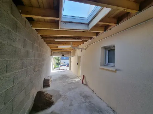 Couloir en construction, partie d'une extension maison, avec murs en parpaings, plafond en bois, fenêtre de toit et matériaux de chantier.