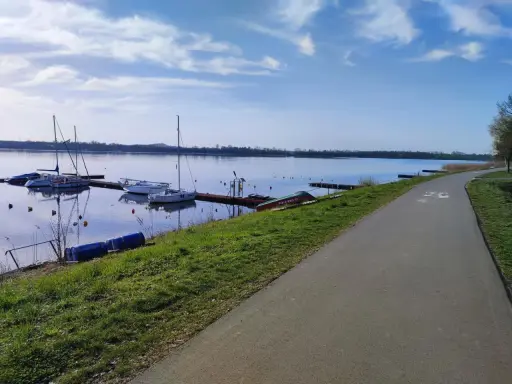 Jezioro Pogoria 4 z łodziami przy pomoście i ścieżką rowerową.