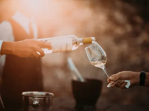 En person häller upp ett glas vin från en flaska. Solen skiner och skapar en varm atmosfär.