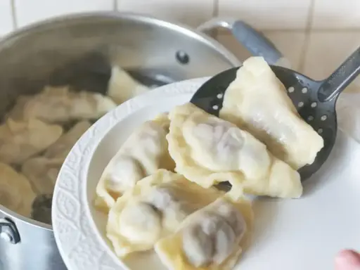 Gotowanie pierogów: gdy wypłyną na powierzchnię, gotuj jeszcze 2-3 minuty. Na talerzu czeka porcja świeżo ugotowanych, parujących pierogów.