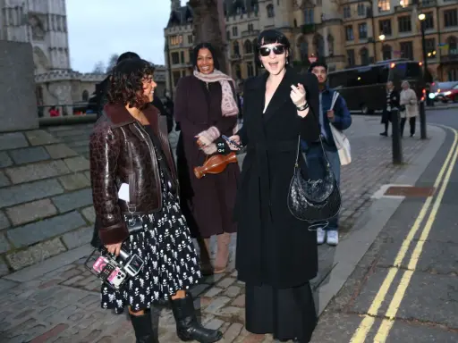 Un elegante cappotto a vestaglia nero, indossato con disinvoltura, si abbina perfettamente a un look audace e moderno.