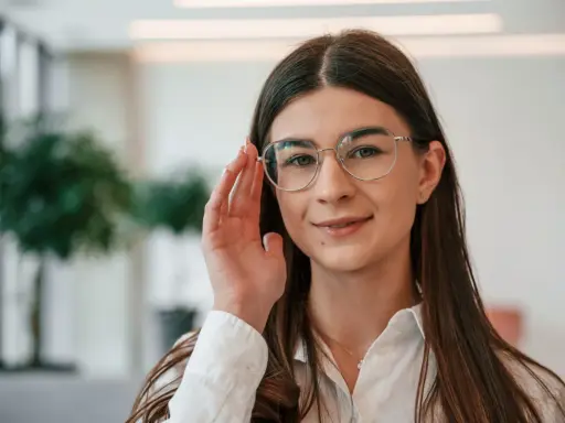 Uśmiechnięta kobieta w okularach do czytania i chodzenia poprawia oprawki.