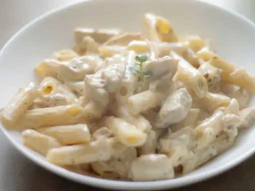 Penne z kremowym sosem i kawałkami kurczaka, udekorowane gałązką ziół. Pyszna potrawka z kurczaka w sam raz na obiad.