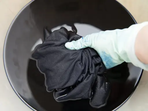 Mano con guante sumerge ropa blanca desteñida de negro en tinte oscuro.
