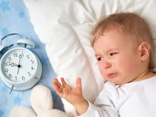 Płacz 1,5 rocznego dziecka, które nie chce spać w dzień. Obok budzik i pluszaki.