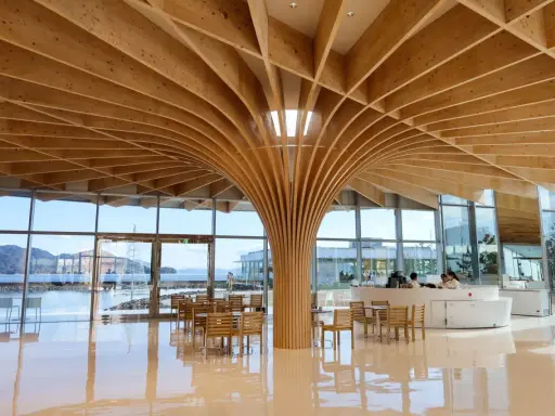 Interno moderno con soffitto in legno curvo, un esempio di architettura giapponese. Tavoli e sedie in legno, vista sul mare.