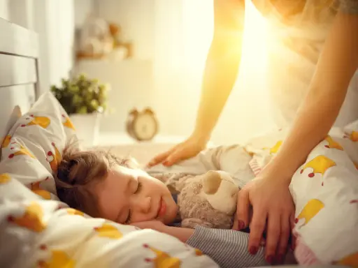Mama pomaga dziecku zasnąć, kładąc rękę na jego ramieniu. Słodki sen malucha to pierwszy krok, jak nauczyć dziecko zasypiać samo.