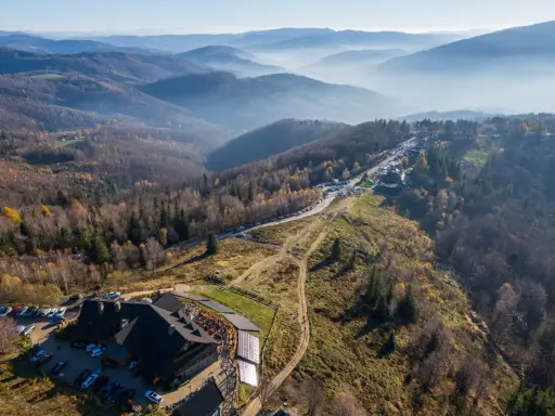 Widok na górskie krajobrazy i architekturę w Ustroniu. Widać parkingi, budynek z drewnianą architekturą i szlaki turystyczne.