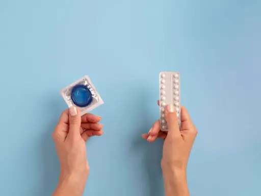 Manos sostienen un preservativo y pastillas anticonceptivas, mostrando opciones de planificación familiar.