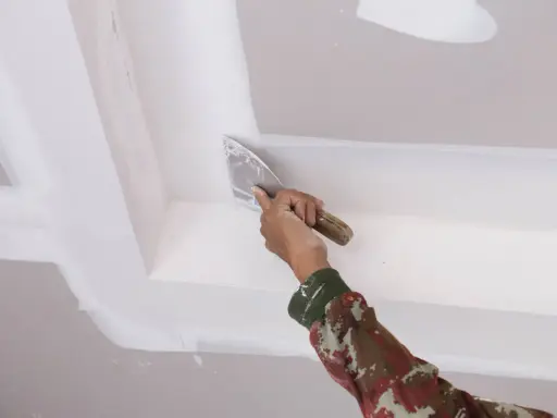 Mano con espátula aplica masilla para reparar techo escayola, dejando un acabado liso y perfecto.