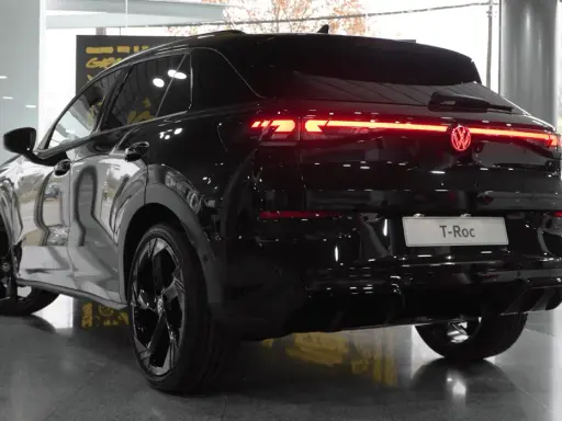 El Volkswagen T-Roc 2026 negro brillante, con sus luces traseras LED rojas encendidas, se exhibe en un concesionario.