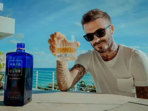 David Beckham z kieliszkiem Haig Club whisky, na tle błękitnego nieba i morza. Idealny moment na relaks.